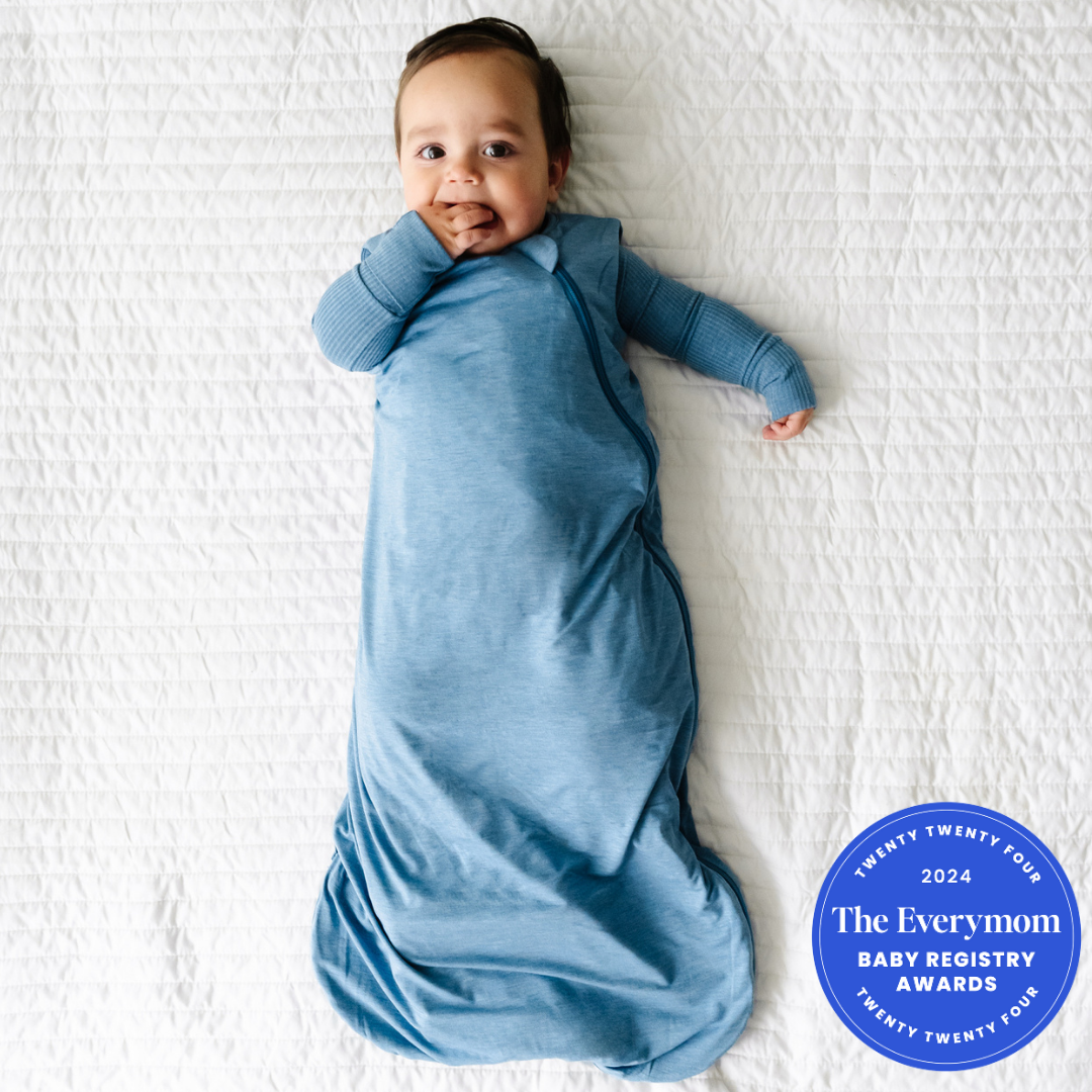 Child laying on a blanket wearing a Heather Blue Sleepy Bag and matching zippy