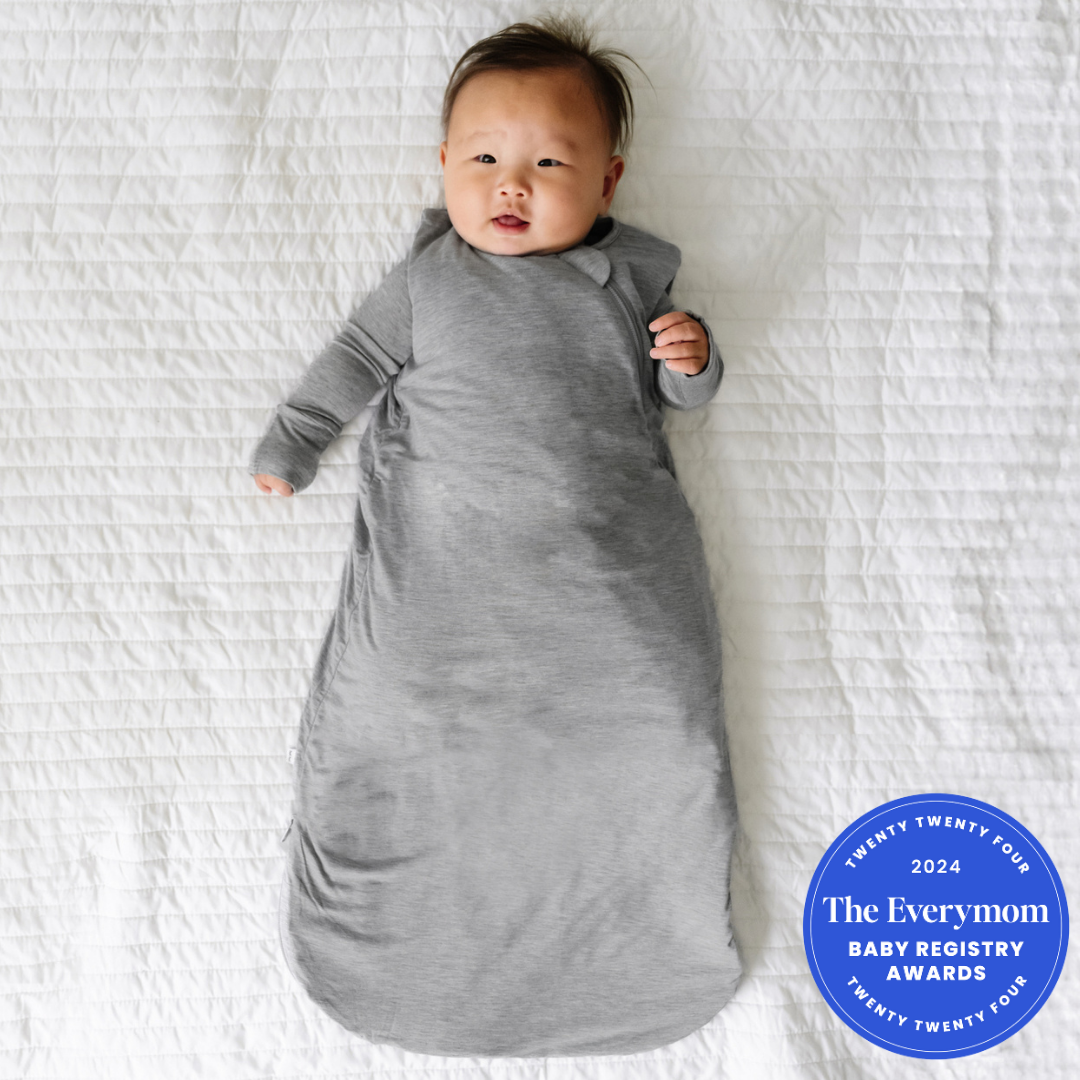 Child laying on a blanket wearing a Heather Gray Sleepy Bag and matching zippy