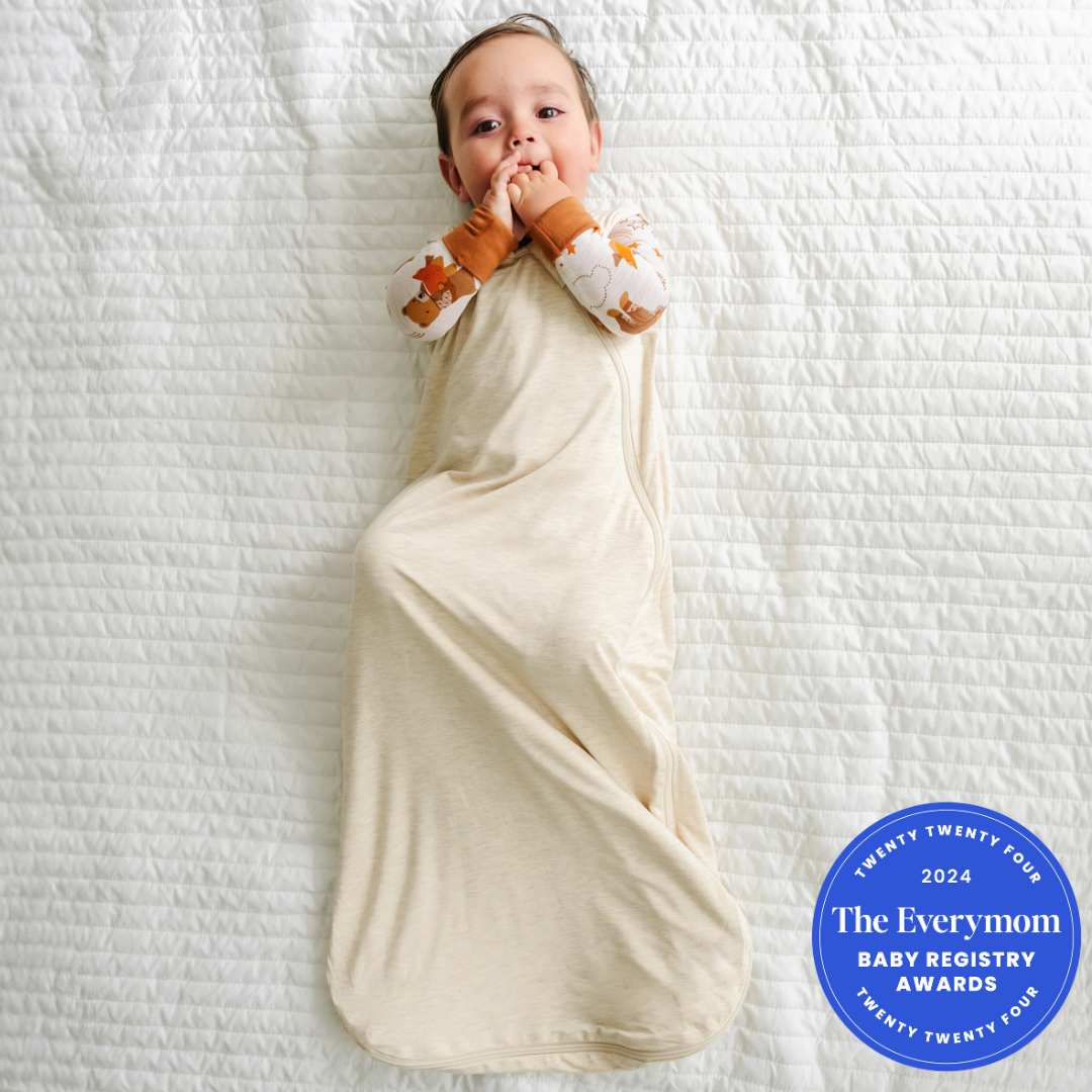 Child laying on a bed wearing a Beary Sleepy zippy in a Heather Oatmeal Sleepy bag