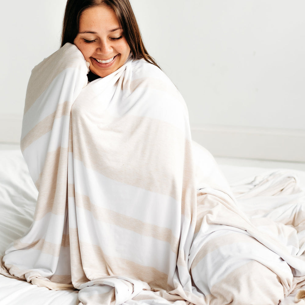 Woman sitting on the ground, wrapped up in a Heather Oatmeal Stripe oversized bamboo blanket