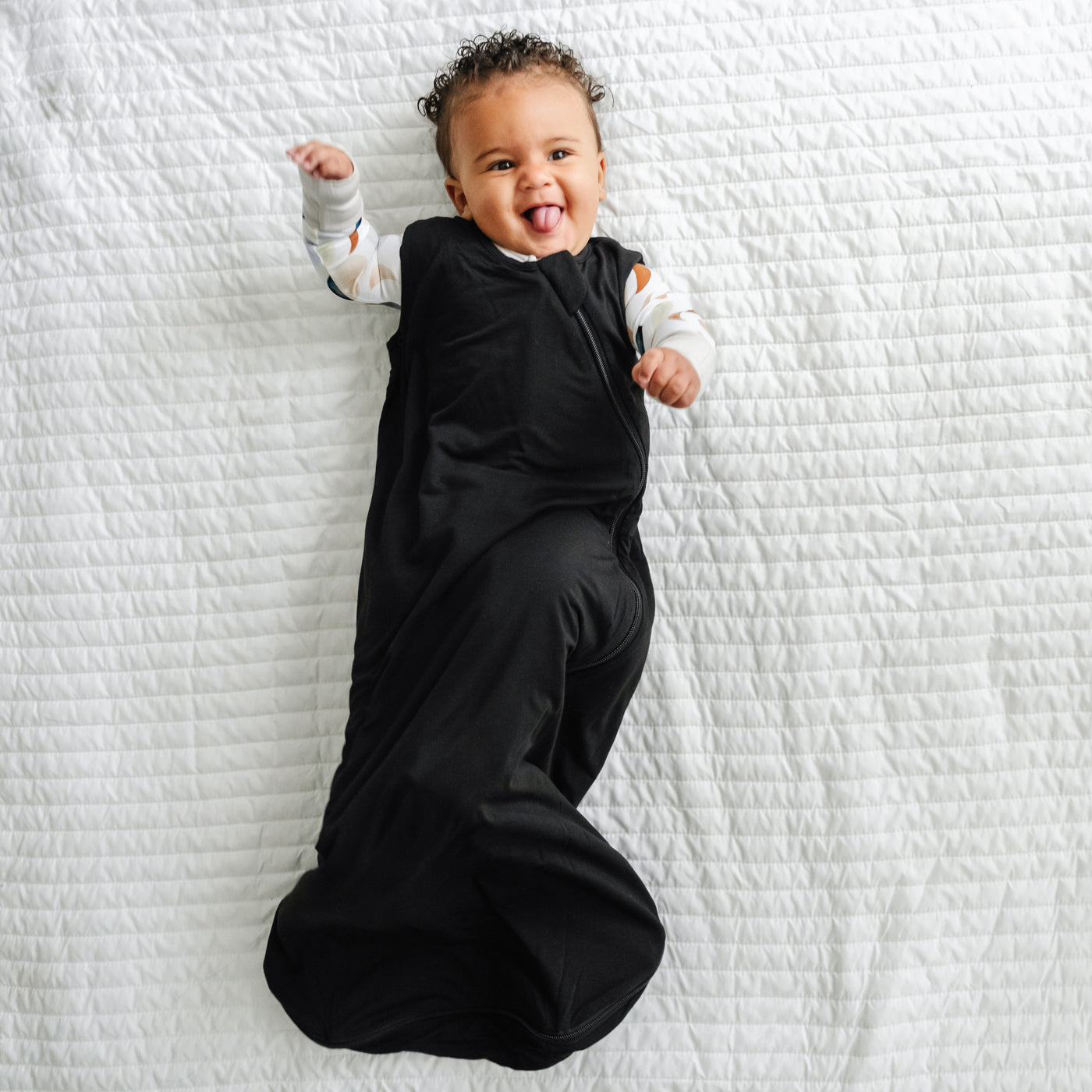 Alternate image of a child laying on a blanket wearing a Black sleepy bag and coordinating zippy