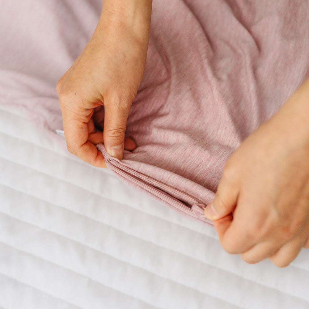 Close up detail image of a parent zipping up a Heather Mauve sleepy bag