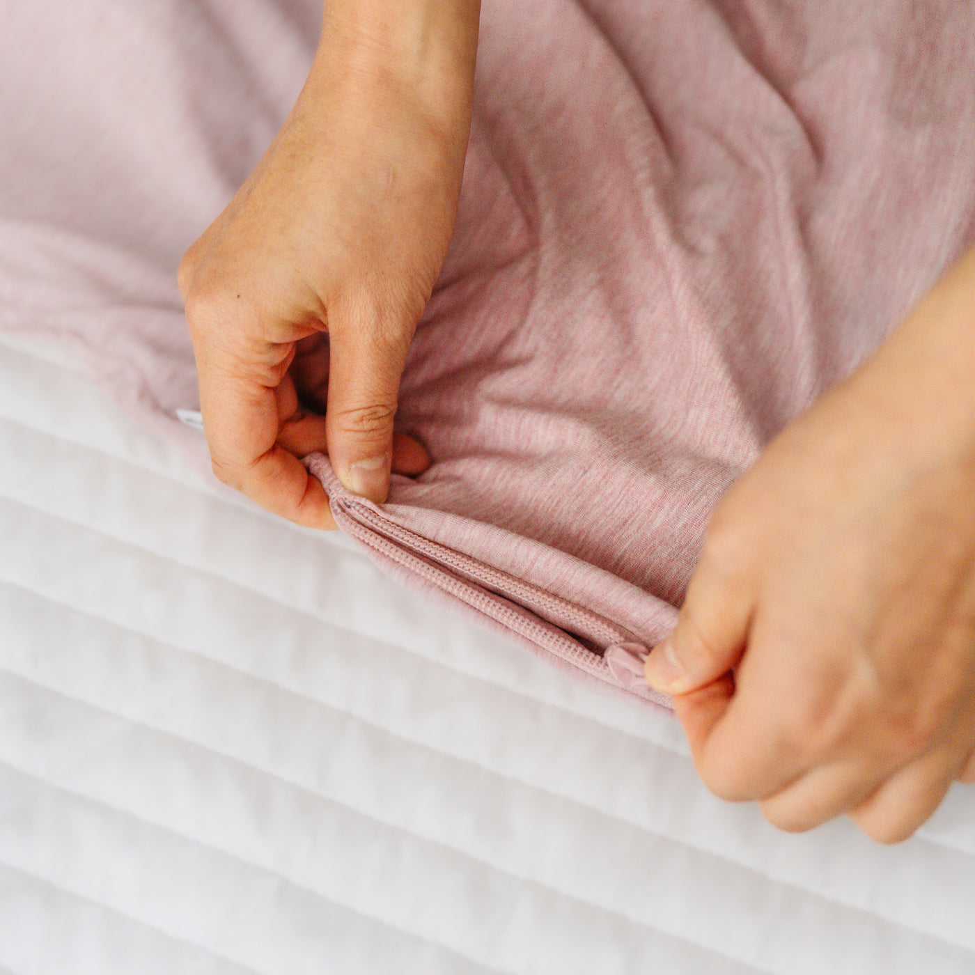 Close up detail image of a parent zipping up a Heather Mauve sleepy bag