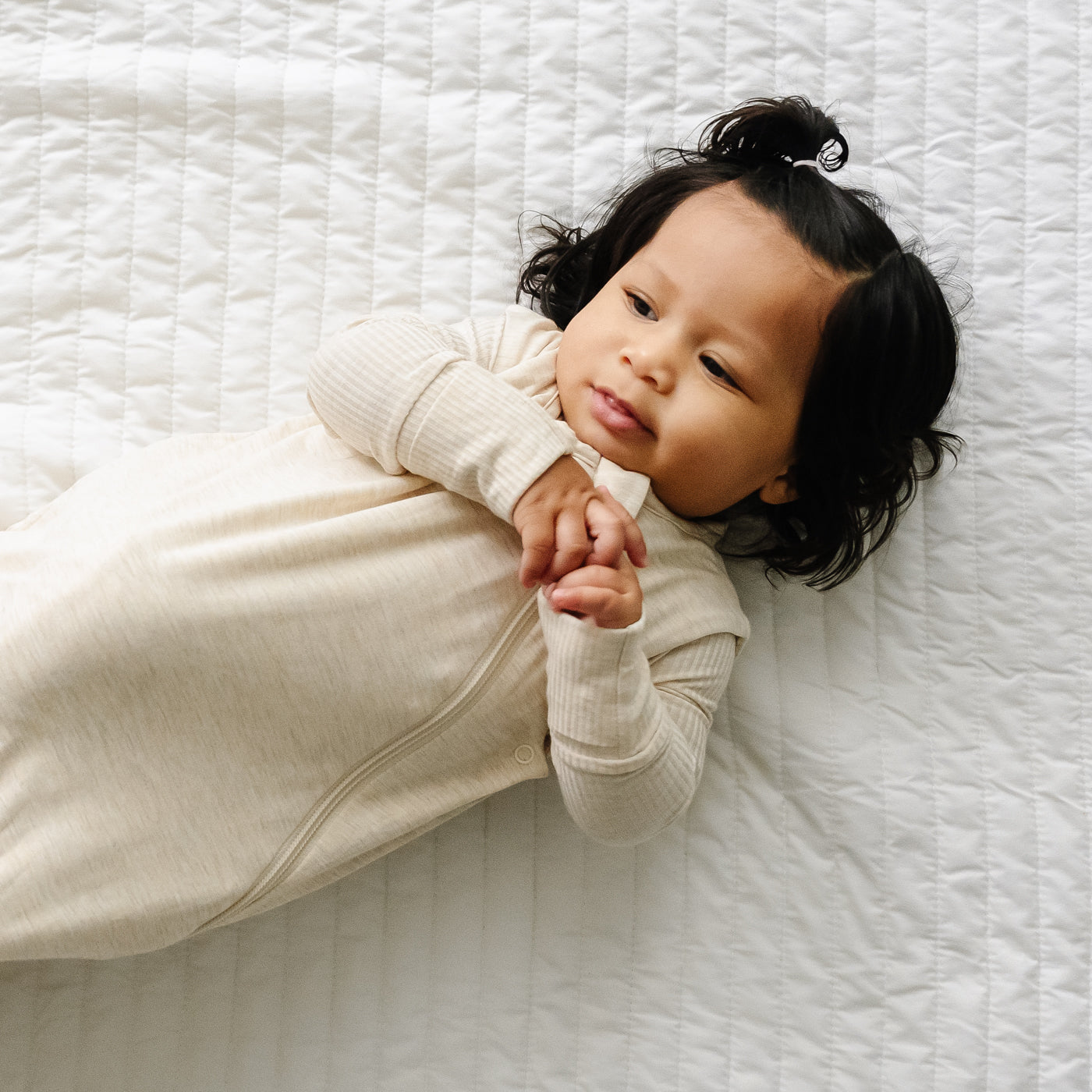 Child laying on a blanket wearing a Heather Oatmeal sleepy bag and matching zippy